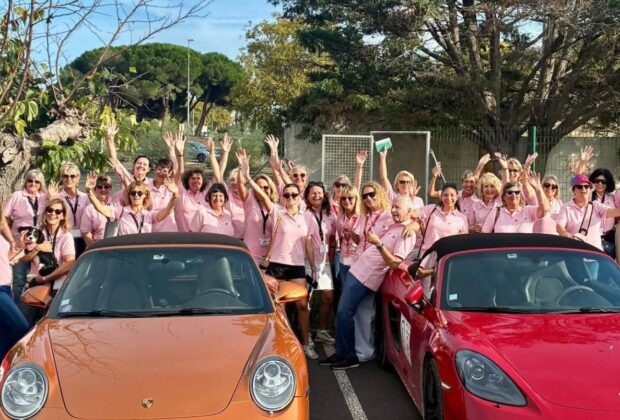 Participantes en polos roses derrière des Porsche orange et rouge au Rallye des Demoiselles.