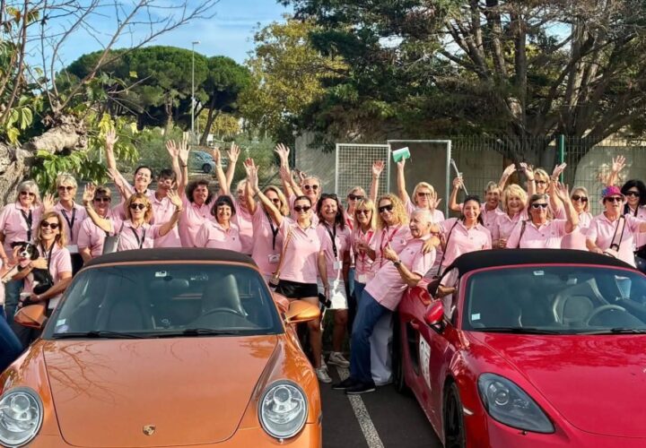 Participantes en polos roses derrière des Porsche orange et rouge au Rallye des Demoiselles.