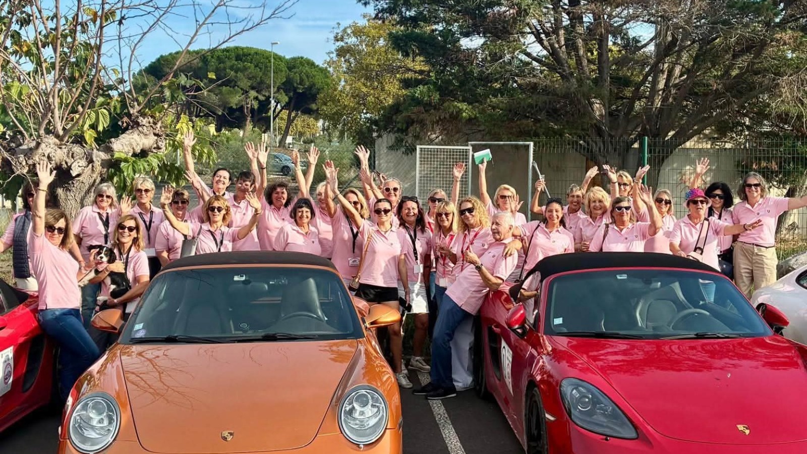 Participantes en polos roses derrière des Porsche orange et rouge au Rallye des Demoiselles.