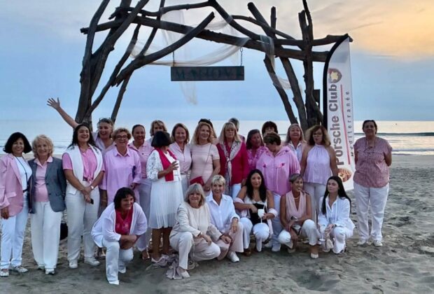 Participantes en tenues roses et blanches réunies sur la plage sous une arche de bois.