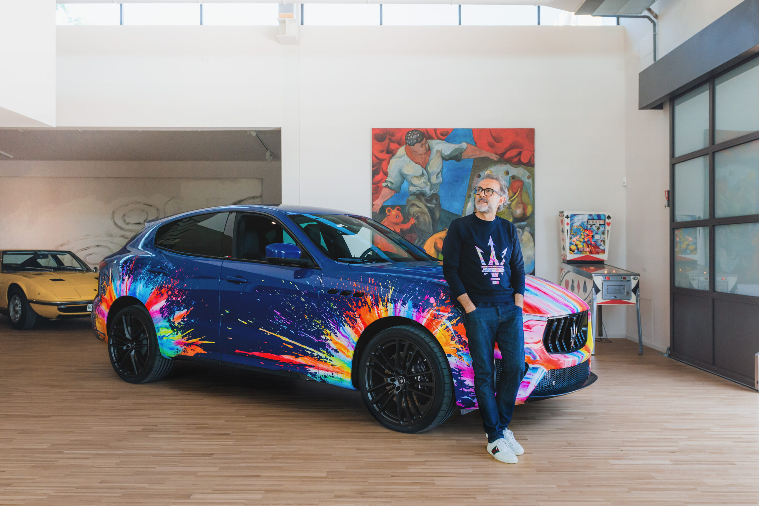 Massimo Bottura debout devant son Maserati Levante Trofeo bleu couvert de projections multicolores